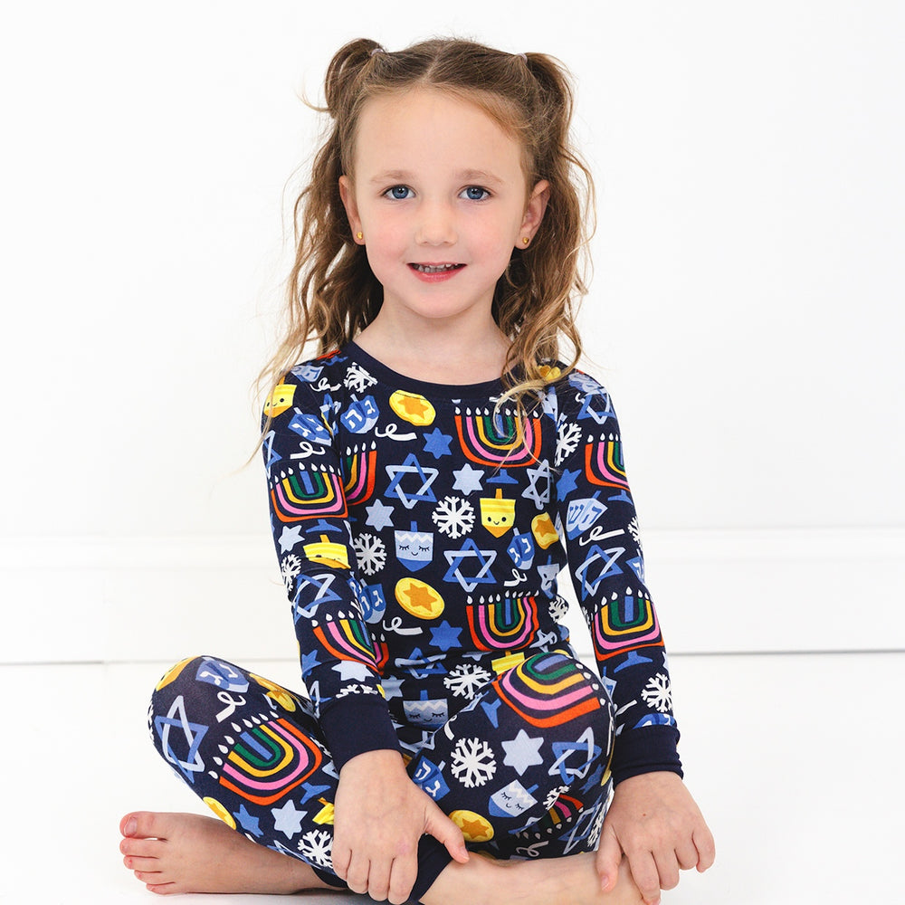 Child sitting on the ground wearing a Playful Dreidels Two-Piece Pajama Set