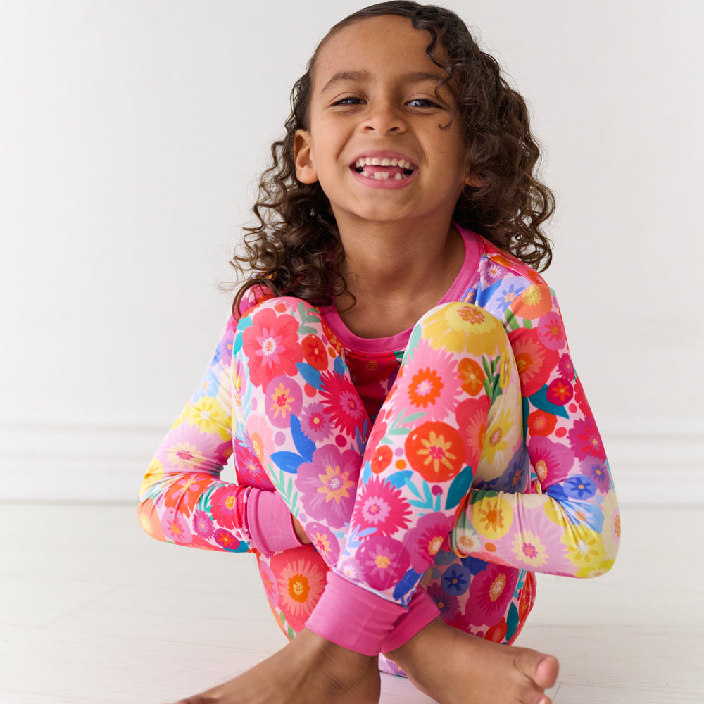 Child sitting on the ground wearing a Rainbow Blooms two-piece pajama set