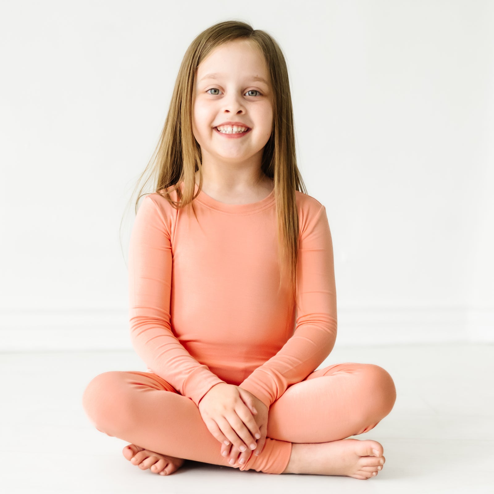 Child sitting wearing a Peach two piece pajama set