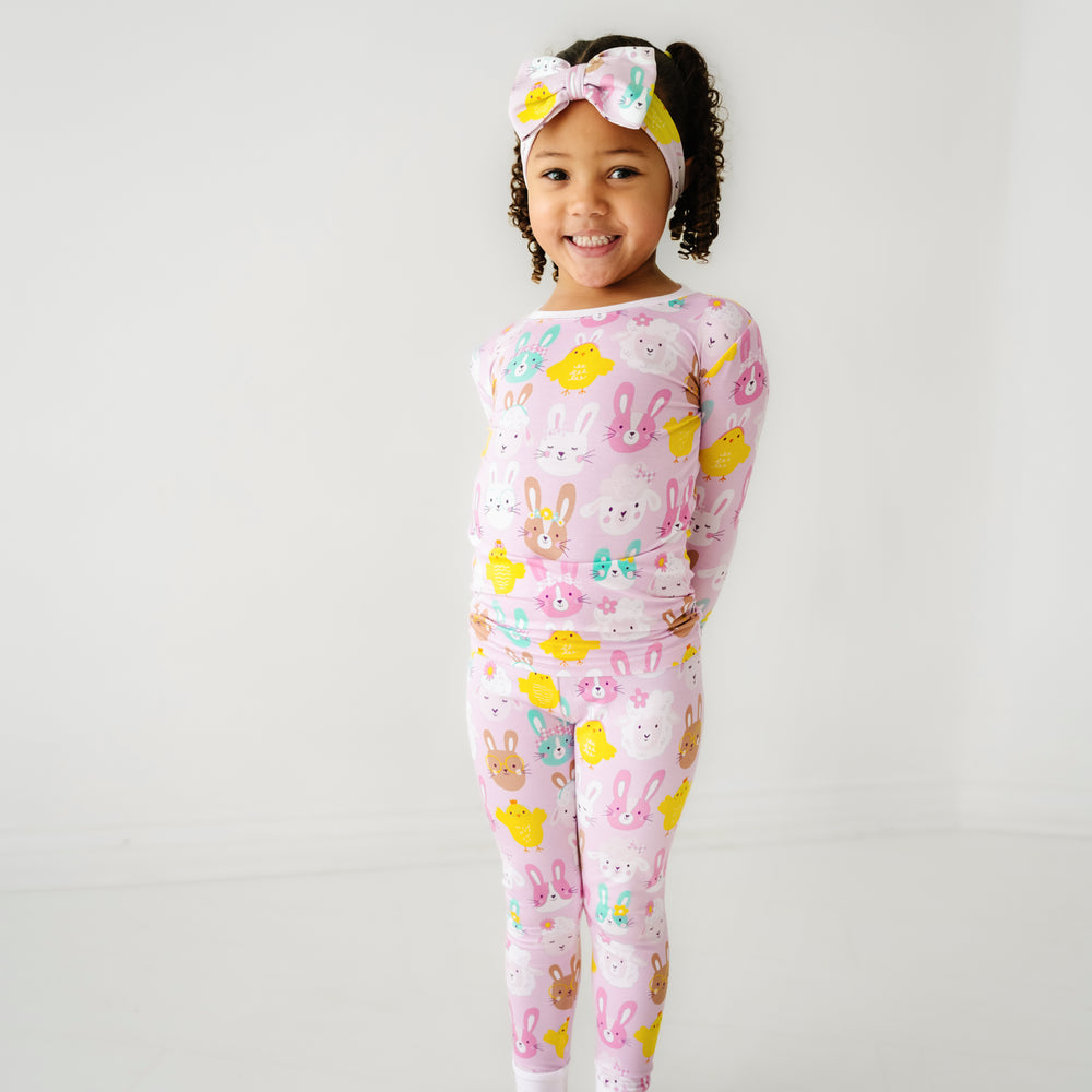 Click to see full screen - Child posing wearing Pink Pastel Parade two piece pajama set paired with a matching luxe bow headband