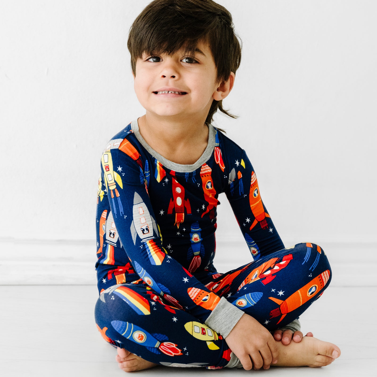 Child sitting wearing a Navy Space Explorer two piece pajama set