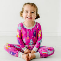 Child sitting wearing a Pink Space Explorer two piece pajama set