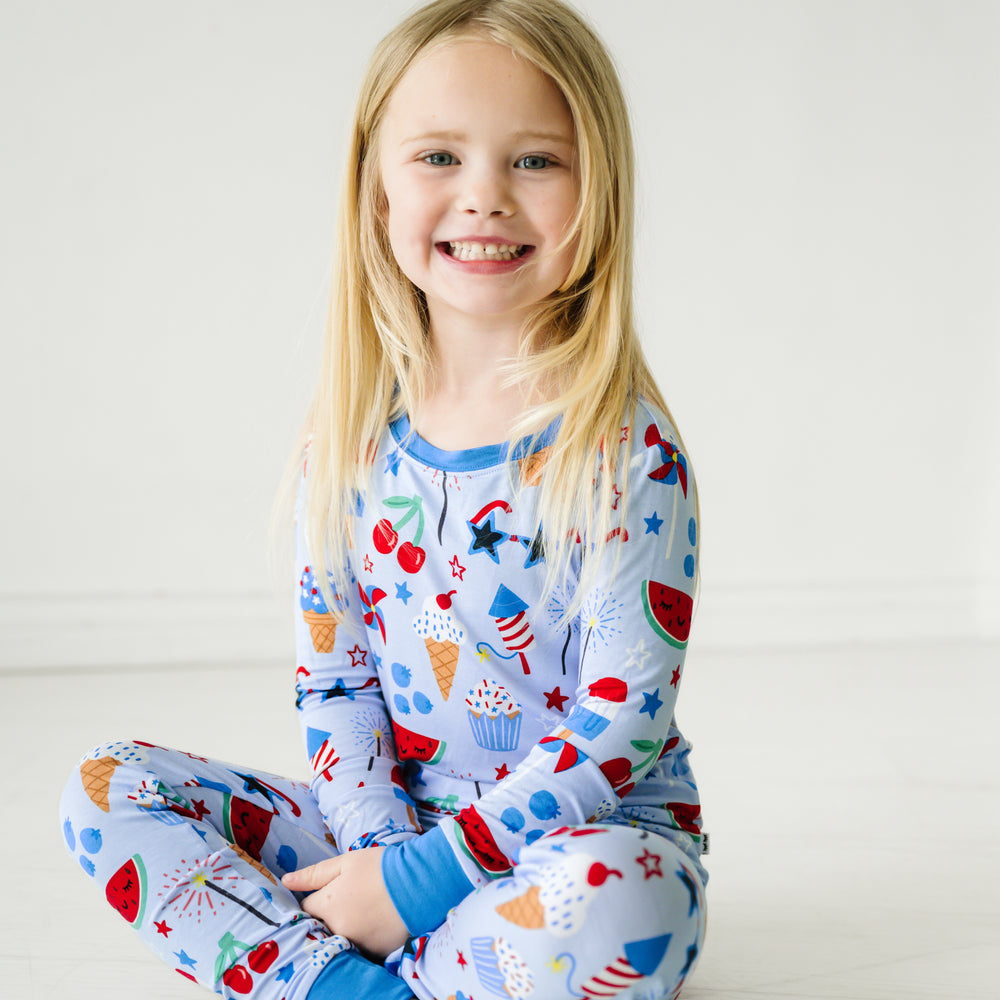 Child sitting wearing a Stars, Stripes, and Sweets two piece pajama set