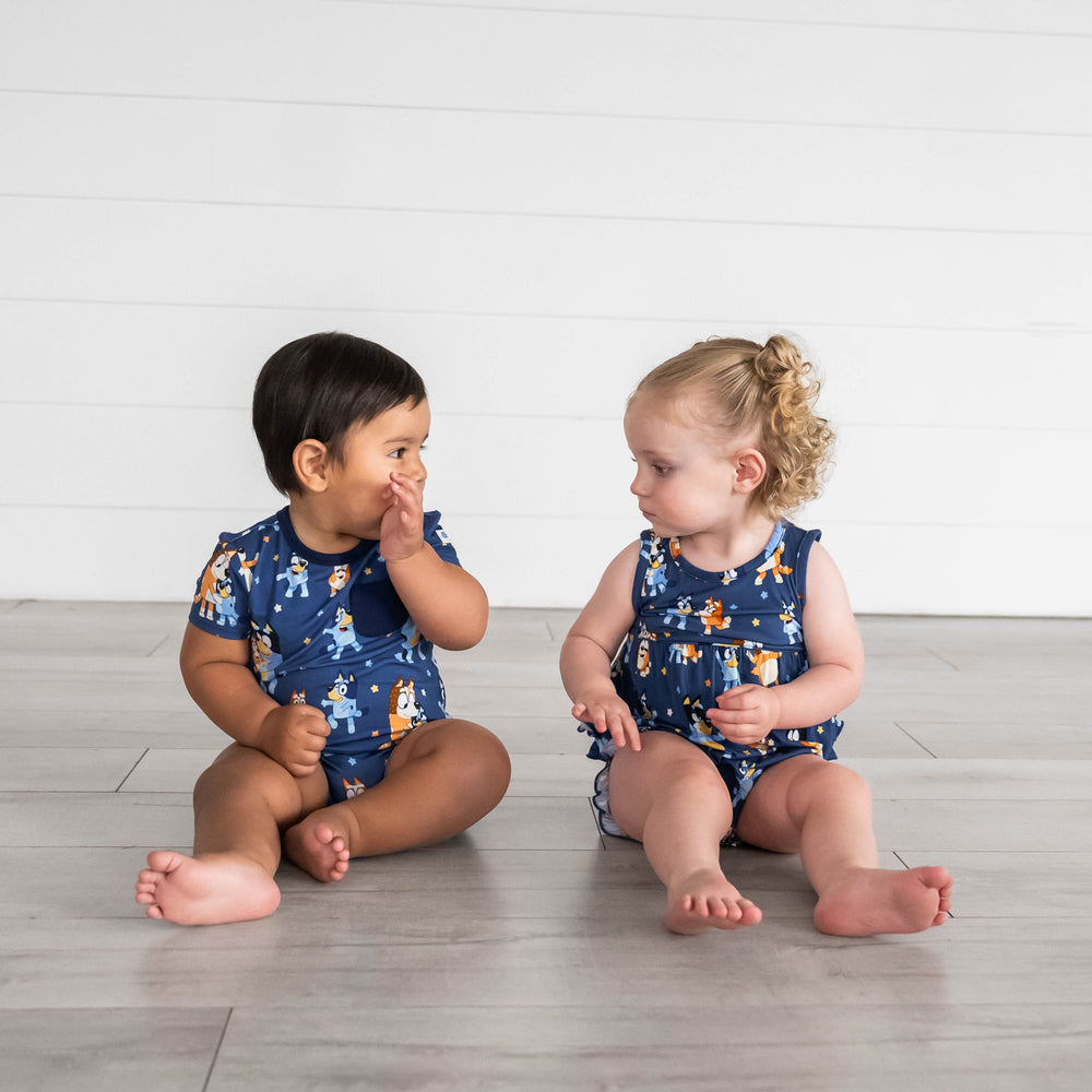 Boy sitting on the left wearing the Bluey Dance Mode Pocket Shorty Romper and girl sitting on the right is wearing the Bluey Dance Mode Bubble Romper