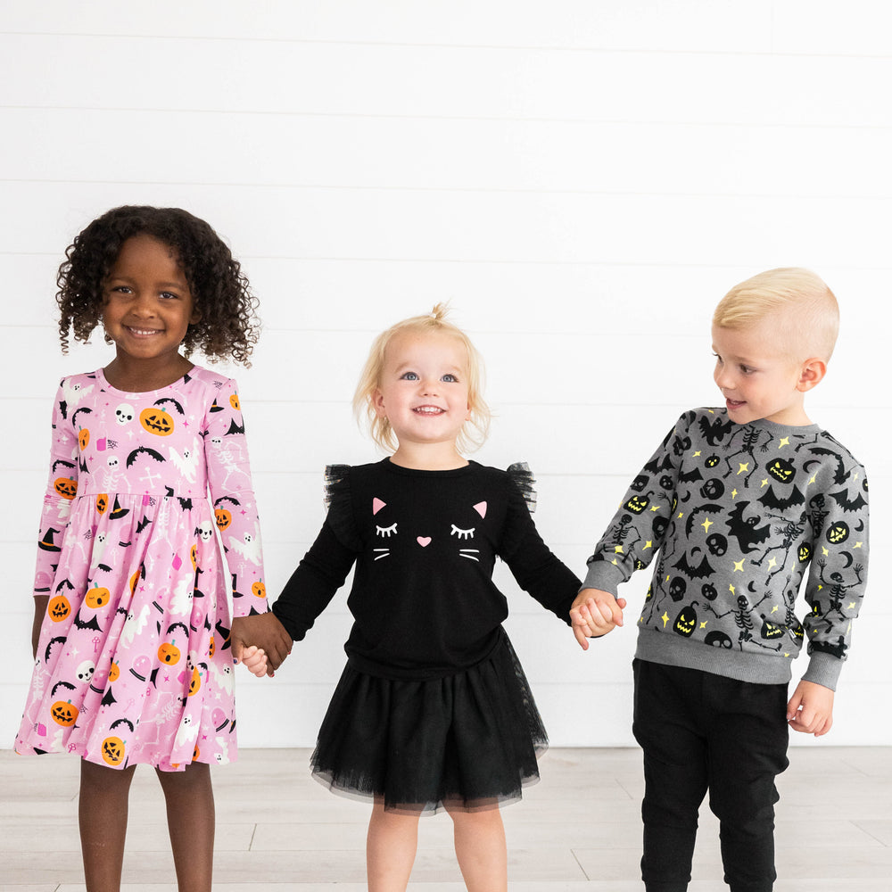 Girl on the left is in the Pink Glowing Ghouls Twirl Dress, girl in the middle is in the Black Tutu Skirt &  Black Cat Flutter Tee, and boy on the left is in the  Gray Glowing Ghouls Crewneck Sweatshirt