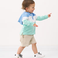 Side view image of a child wearing an Ocean Waves pullover hoodie and coordinating Play shorts