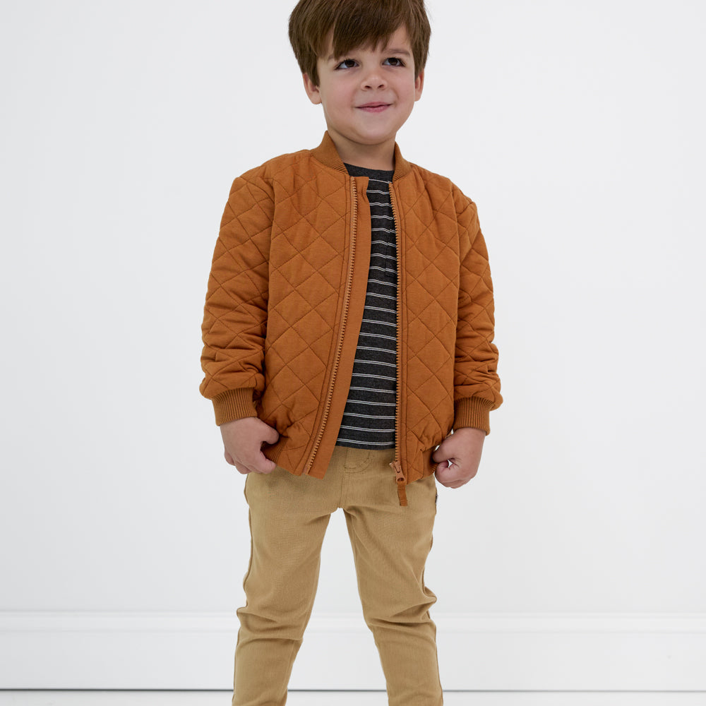 Child looking up wearing a Golden Brown quilted varsity jacket paired with a black striped tee and tan denim joggers