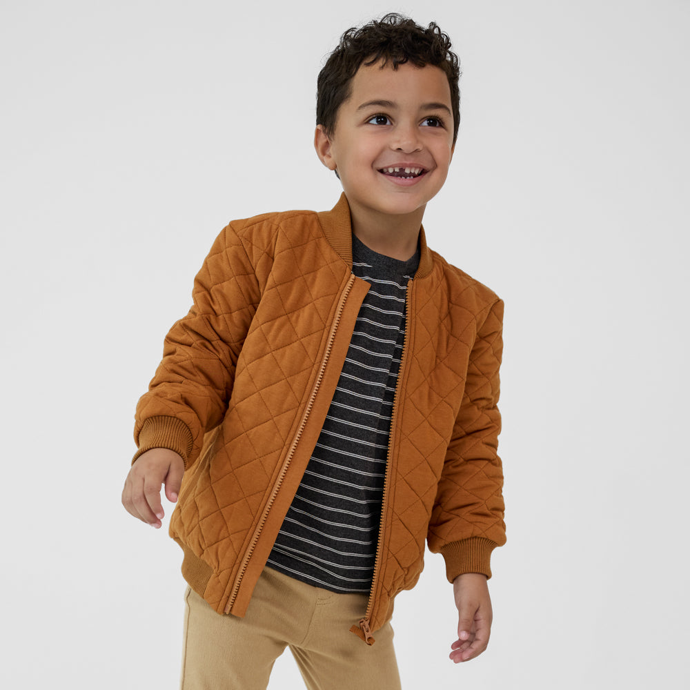 Child wearing a Golden Brown quilted varsity jacket paired with a black striped tee and tan denim joggers