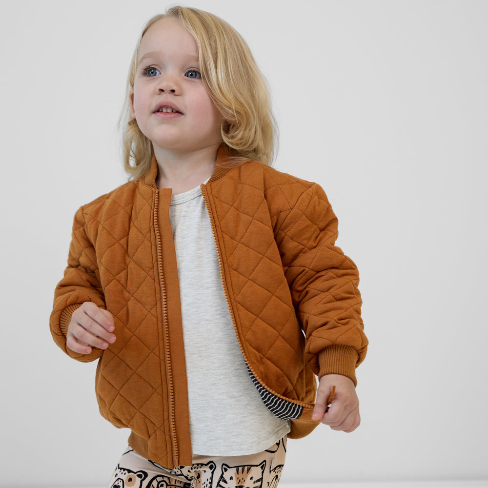 Child wearing a Golden Brown quilted varsity jacket paired with a gray tee and tan animal print leggings