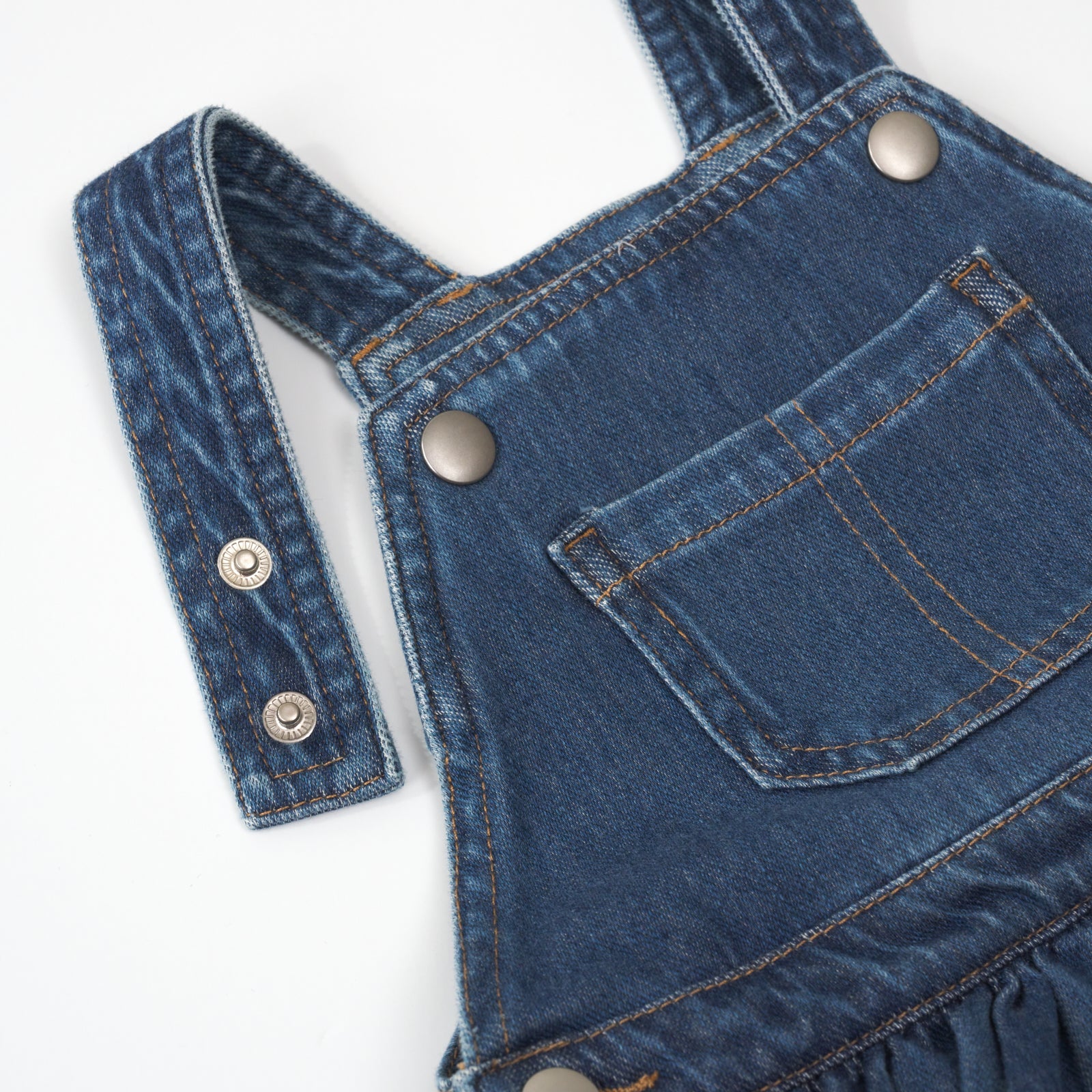 close up view of the straps on a midwash blue denim tiered skirt overall