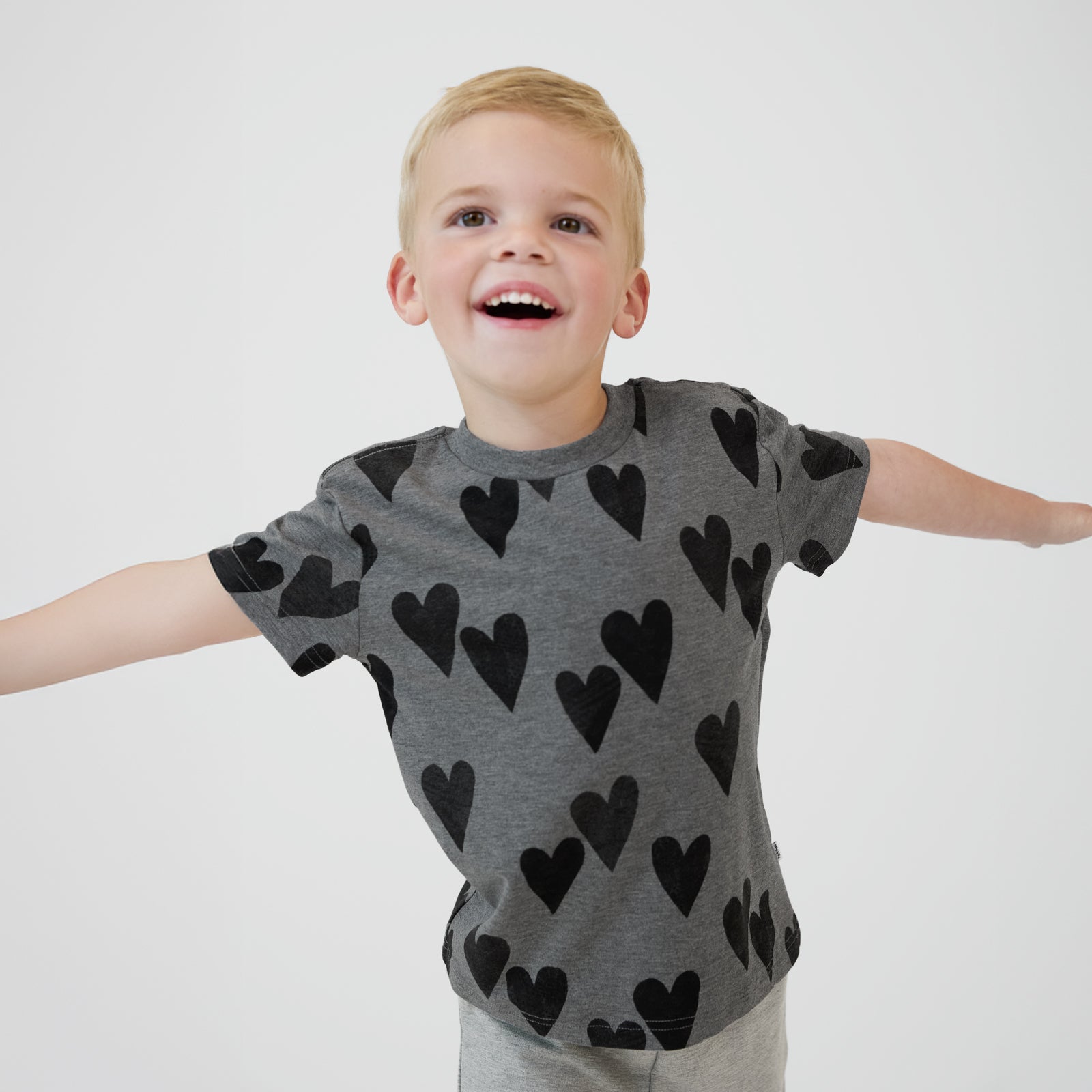 Smiling child with their arms out to the side wearing a Heather Hearts Relaxed Tee