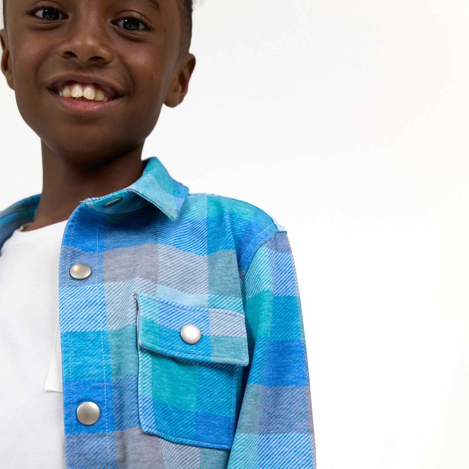 Close up image of smiling boy wearing the Arctic Plaid Shacket, detailing the chest pocket and snap buttons