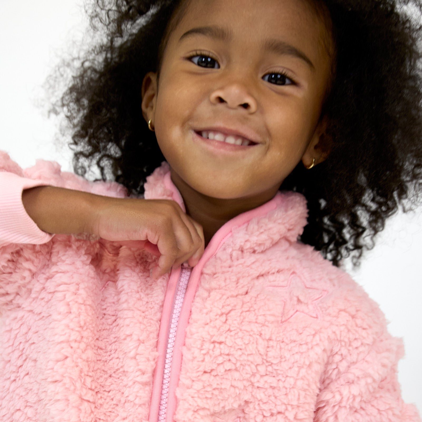 Close up image of smiling girl wearing the Prima Pink Sherpa Zip Jacket and the embroidered star detail on the left chest