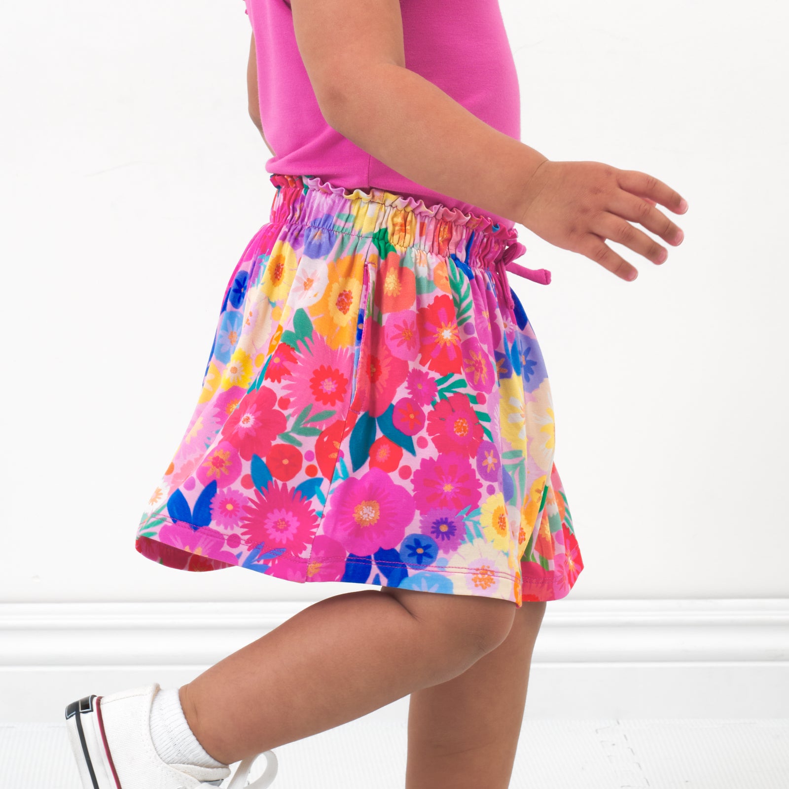 Close up side view image of a child wearing a Rainbow Blooms skort and coordinating top