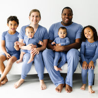 A family of six wearing matching Slate blue pajamas. Mom is wearing women's Slate blue women's pj top and matching women's pj pants. Dad is wearing men's Slate Blue pajama top and matching men's pajama pants. His children are wearing Slate Blue pajamas in two piece and zippy styles