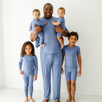A father and his four children wearing matching Slate blue pajamas. dad is wearing men's Slate Blue pajama top and matching men's pajama pants. His children are wearing Slate Blue pajamas in two piece and zippy styles