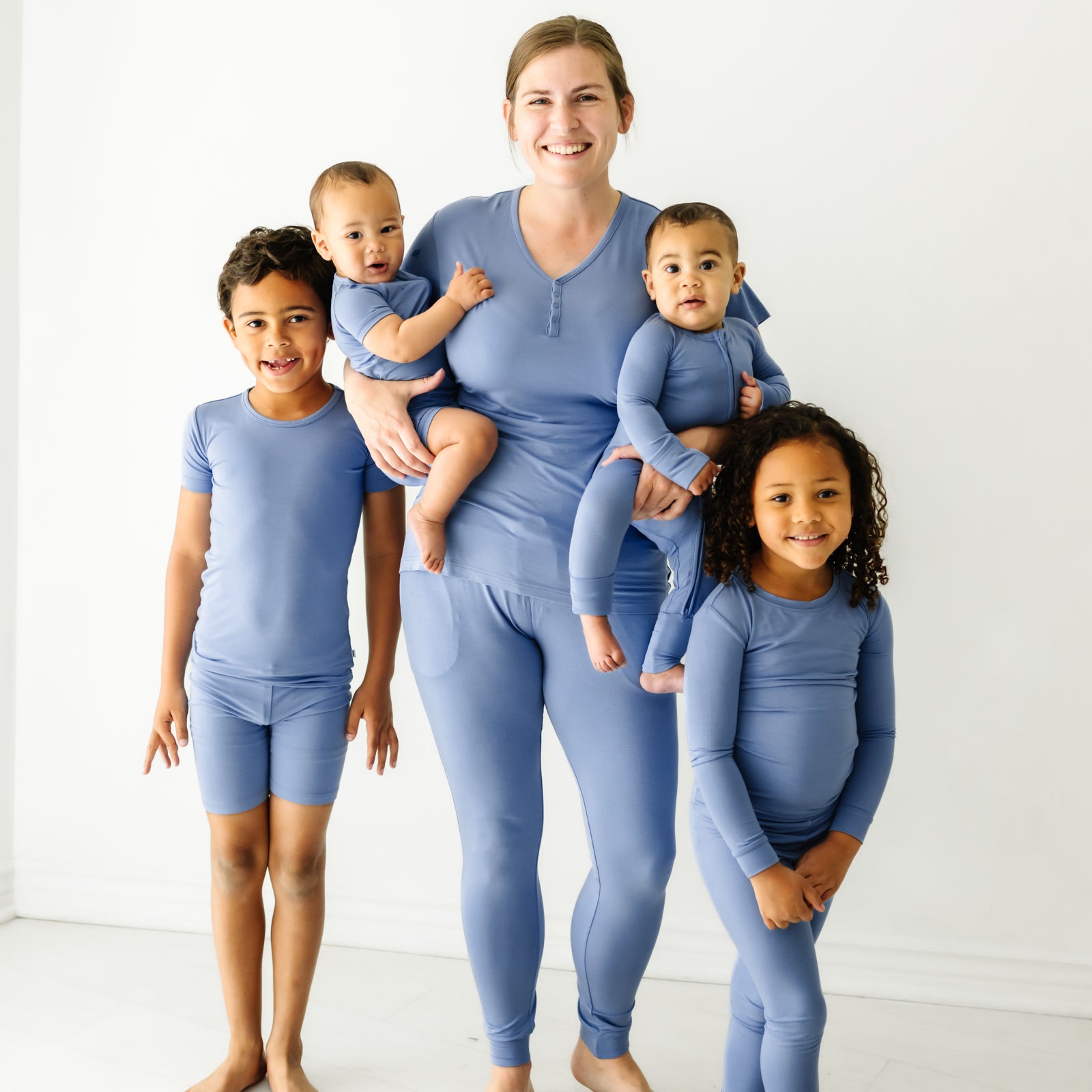 A mother and her four children wearing matching Slate blue pajamas. Mom is wearing women's Slate Blue pajama top and matching women's pajama pants. Her children are wearing Slate Blue pajamas in two piece and zippy styles