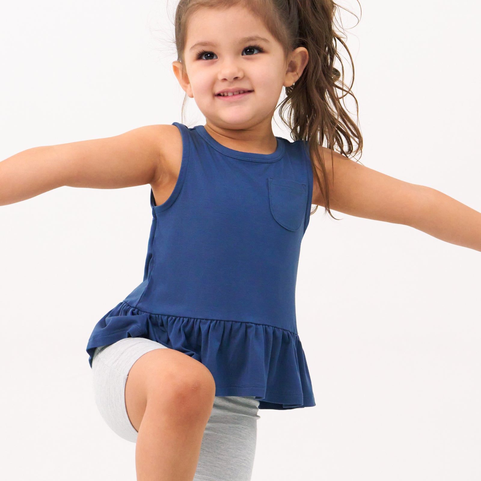 Close up image of a child wearing a Vintage Navy peplum pocket tank and coordinating bike shorts