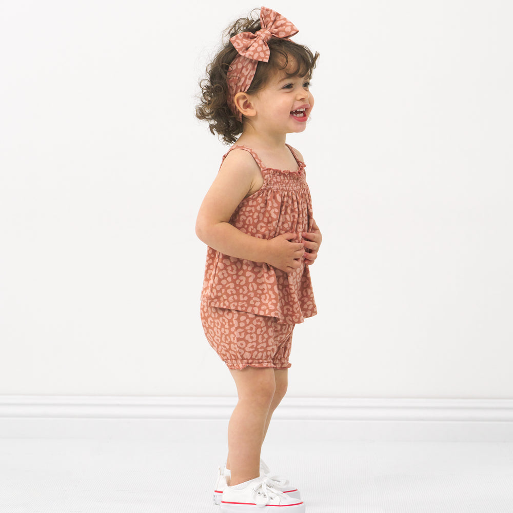 Side view image of a child wearing a Desert Leopard smocked top with shorty bloomer and matching luxe bow headband