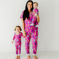 Mother and her two children wearing matching Pink Space Explorer pajama sets. Mom is wearing a women's Pink Space Explorer pajama top and matching pajama pants. Her children are wearing Pink Space Explorer pajamas in two piece and zippy styles