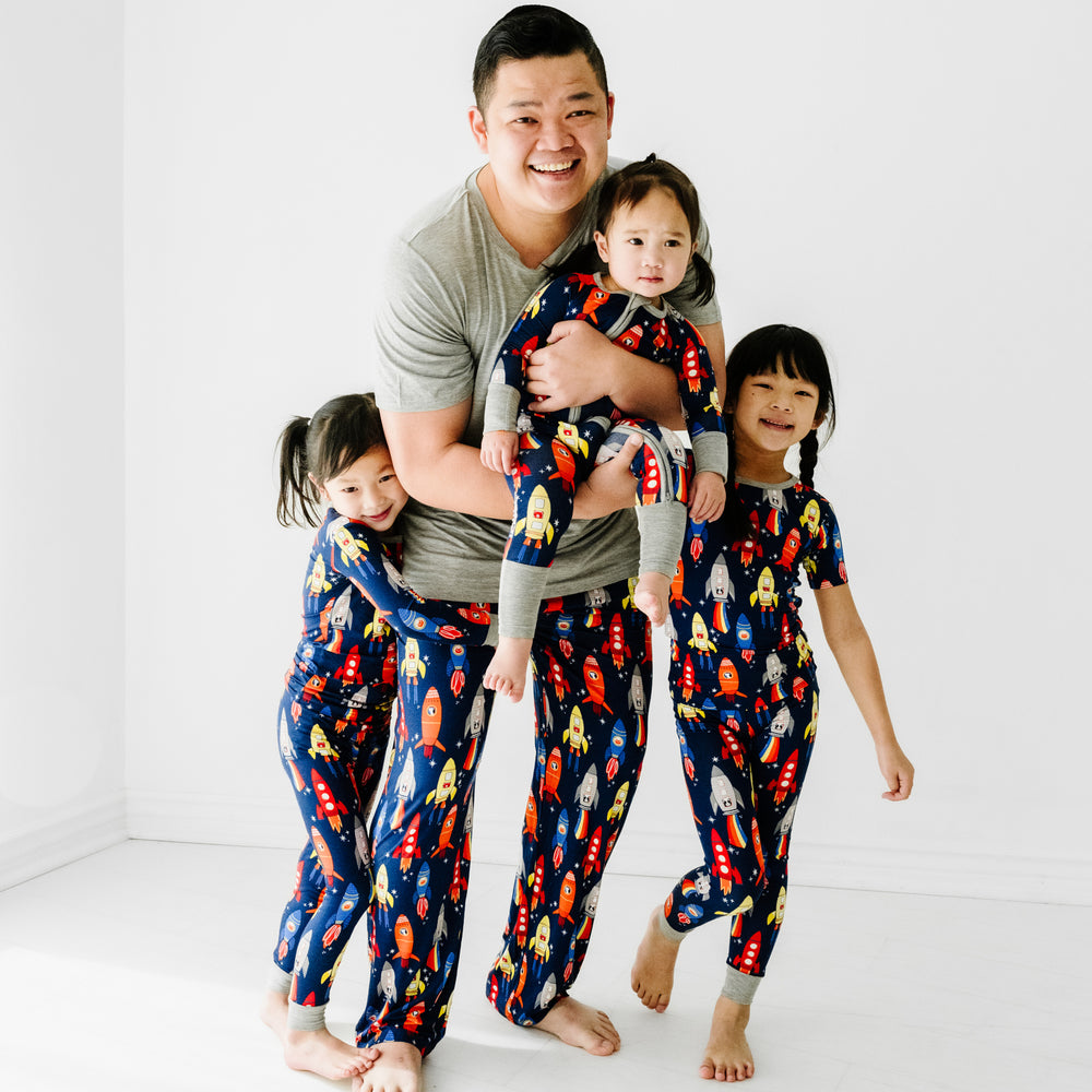 Father and his three children matching wearing Navy Space Explorer pajamas. Dad is wearing men's Navy Space explorer pajama pants paired with a Heather Gray men's pajama top. His kids are wearing Navy Space Explorer pajamas in two piece and zippy styles