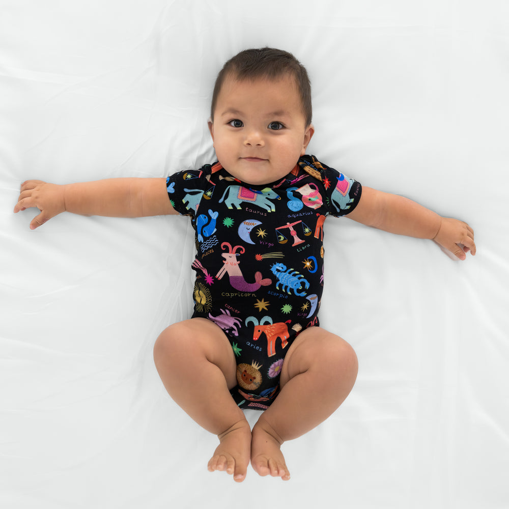 infant lying on a white blanket wearing a star signs bodysuit