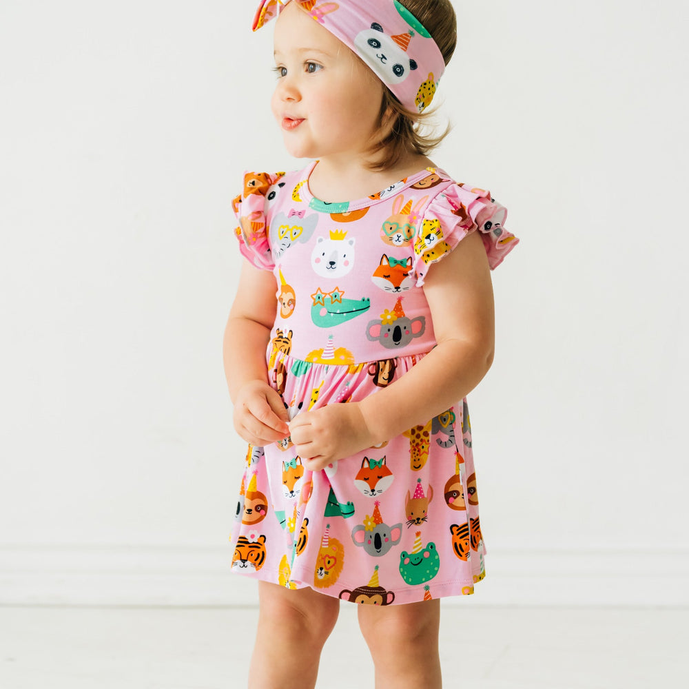 Close up image of a child wearing a Pink Party Animals flutter skater dress with bodysuit and matching luxe bow headband