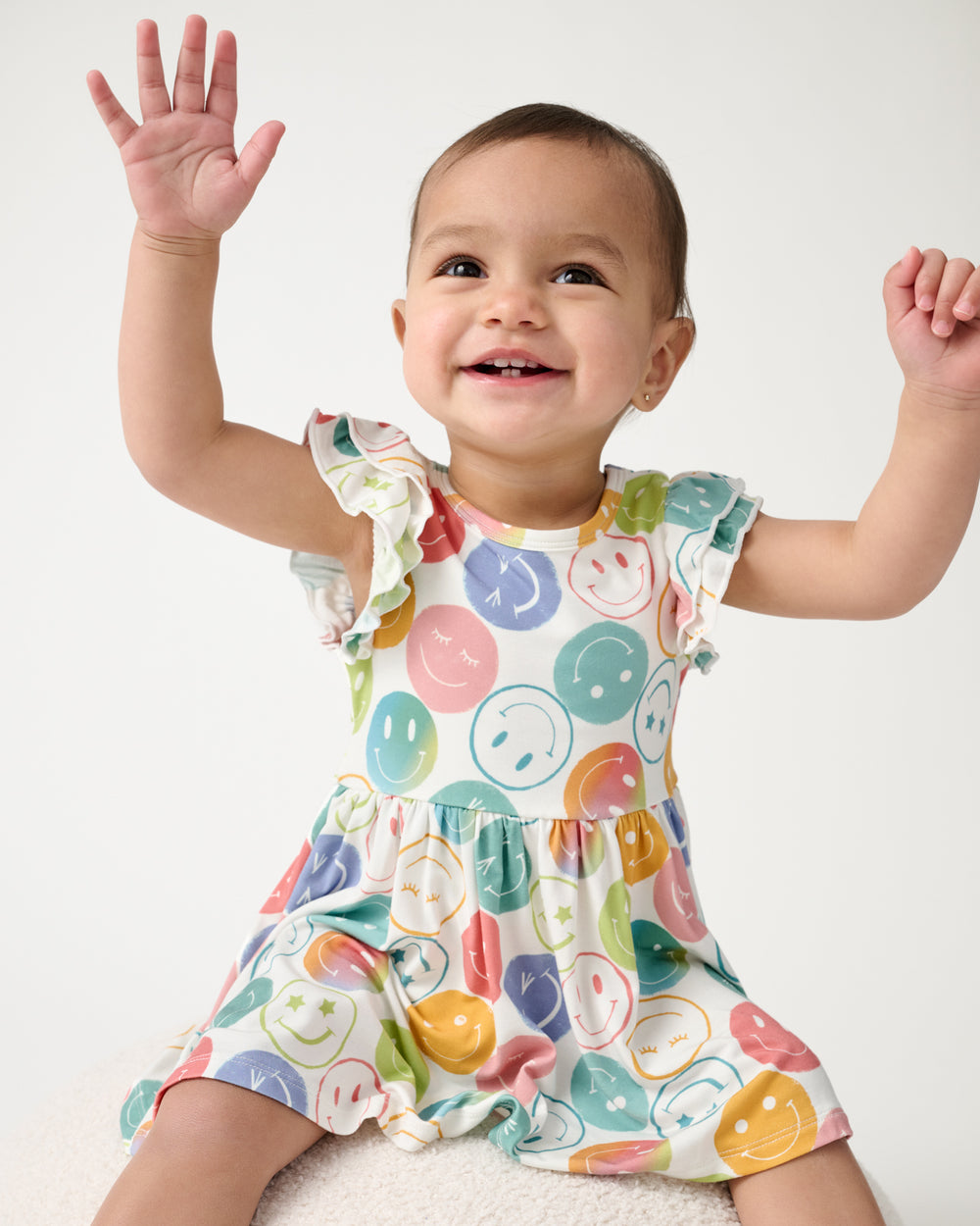 Baby sitting on a white ottoman wearing the Positive Vibes Flutter Twirl Dress with Bodysuit