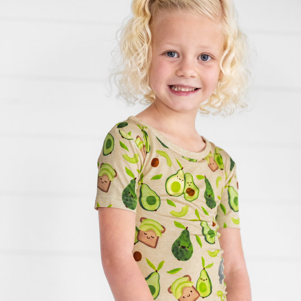 Close up image of a child sitting wearing an Avocado Toast two piece short sleeve pj set