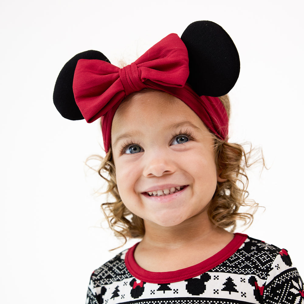 close up image of a child wearing a Minnie Ears luxe bow headband with a Mickey Fair isle pj set