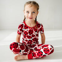 Child sitting on the ground wearing a Love Bug printed two-piece short sleeve pajama set