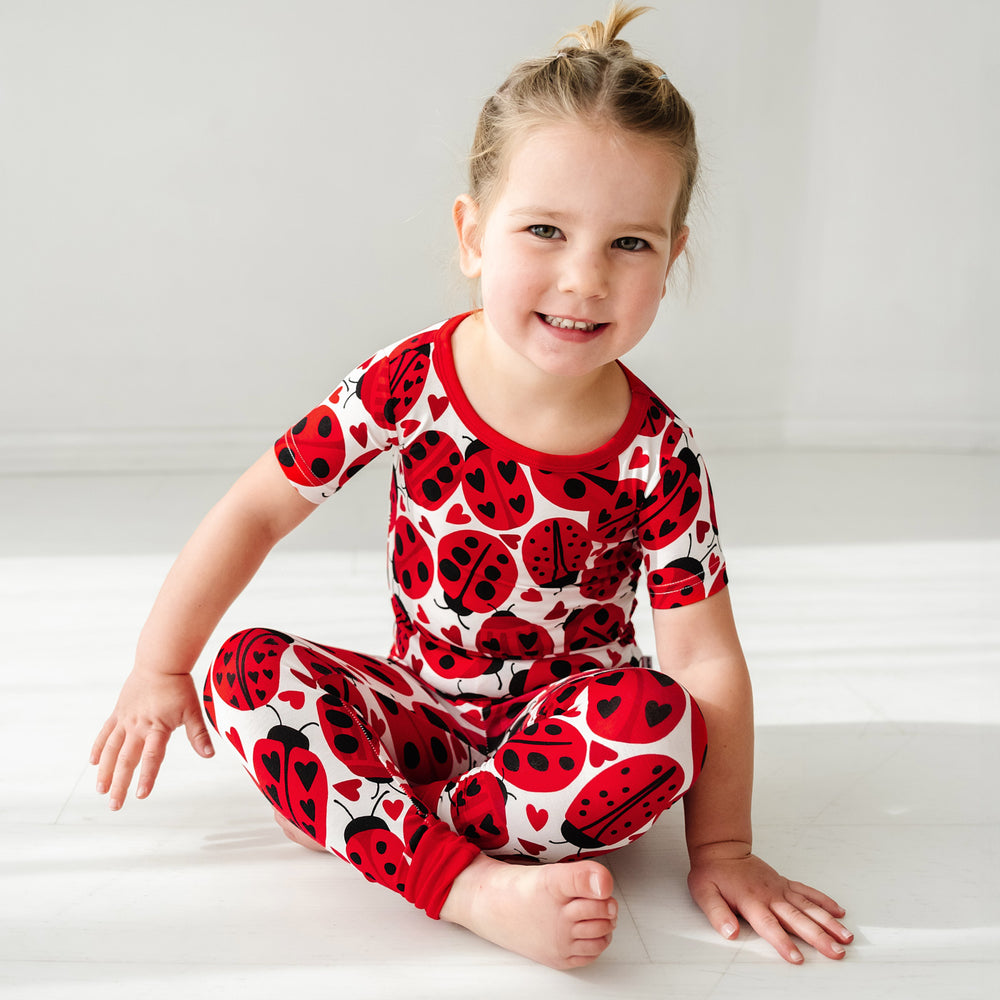 Click to see full screen - Alternate image of a child sitting on the ground wearing a Love Bug printed two-piece short sleeve pajama set