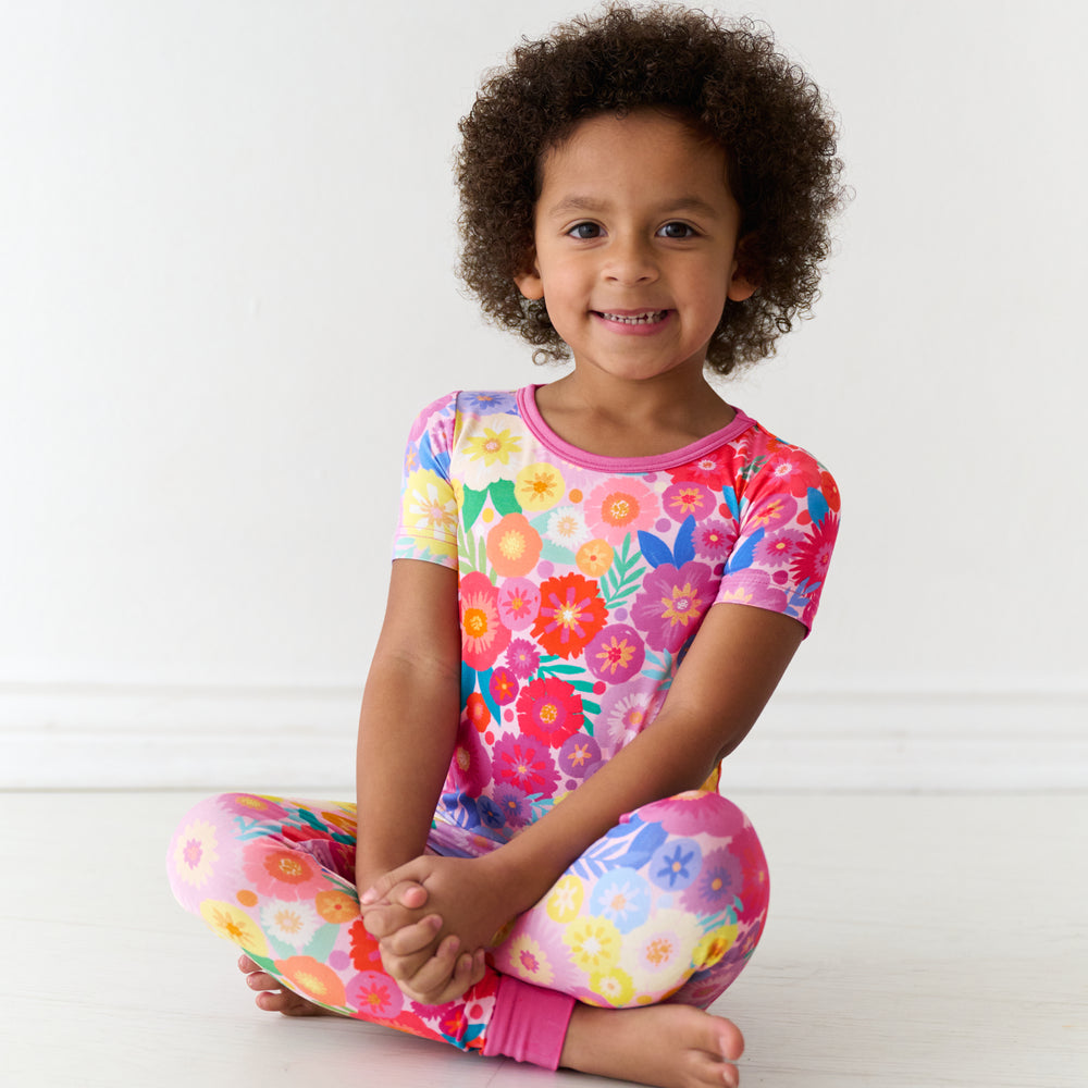 Child sitting on the ground wearing a Rainbow Blooms two-piece short sleeve pajama set