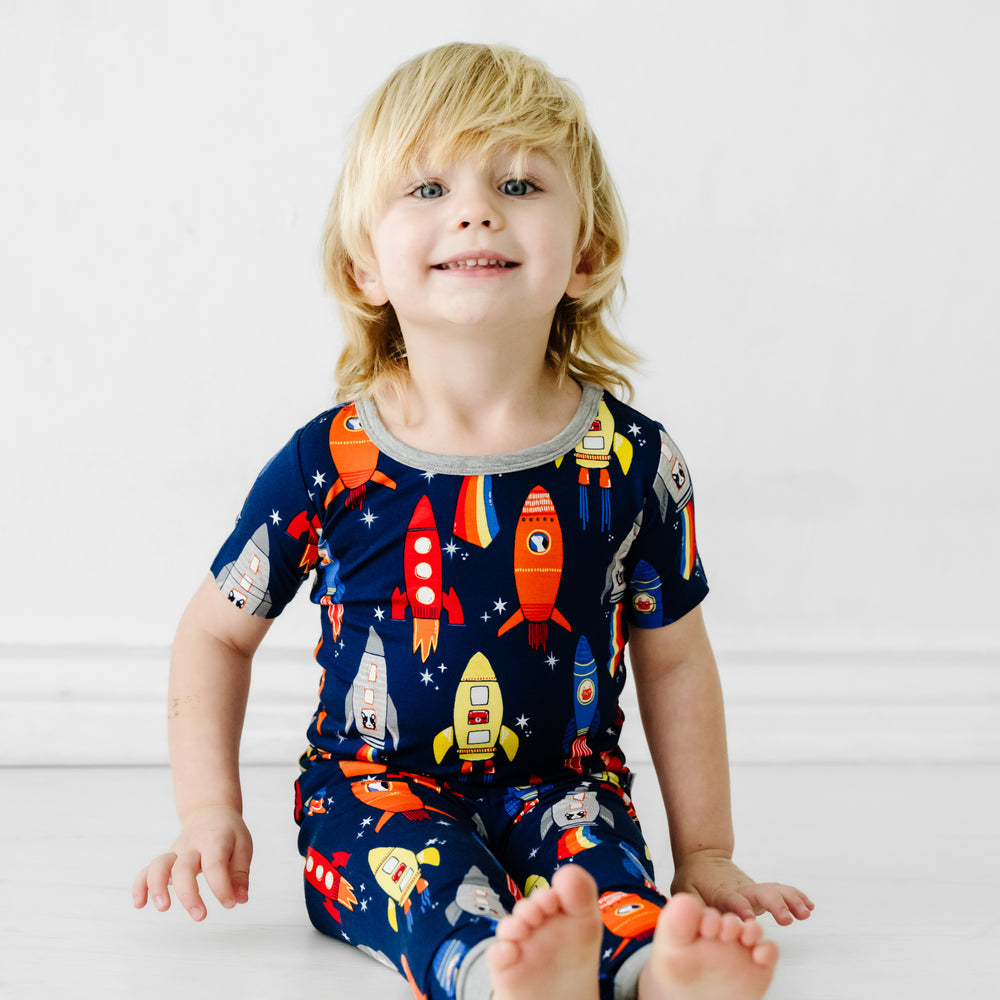 Child sitting wearing a Navy Space Explorer two piece short sleeve pajama set