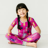 Child sitting wearing a Pink Space Explorer two piece. short sleeve pajama set