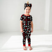 Child wearing Black XOXO two piece short sleeve pajama set paired with a matching luxe bow headband