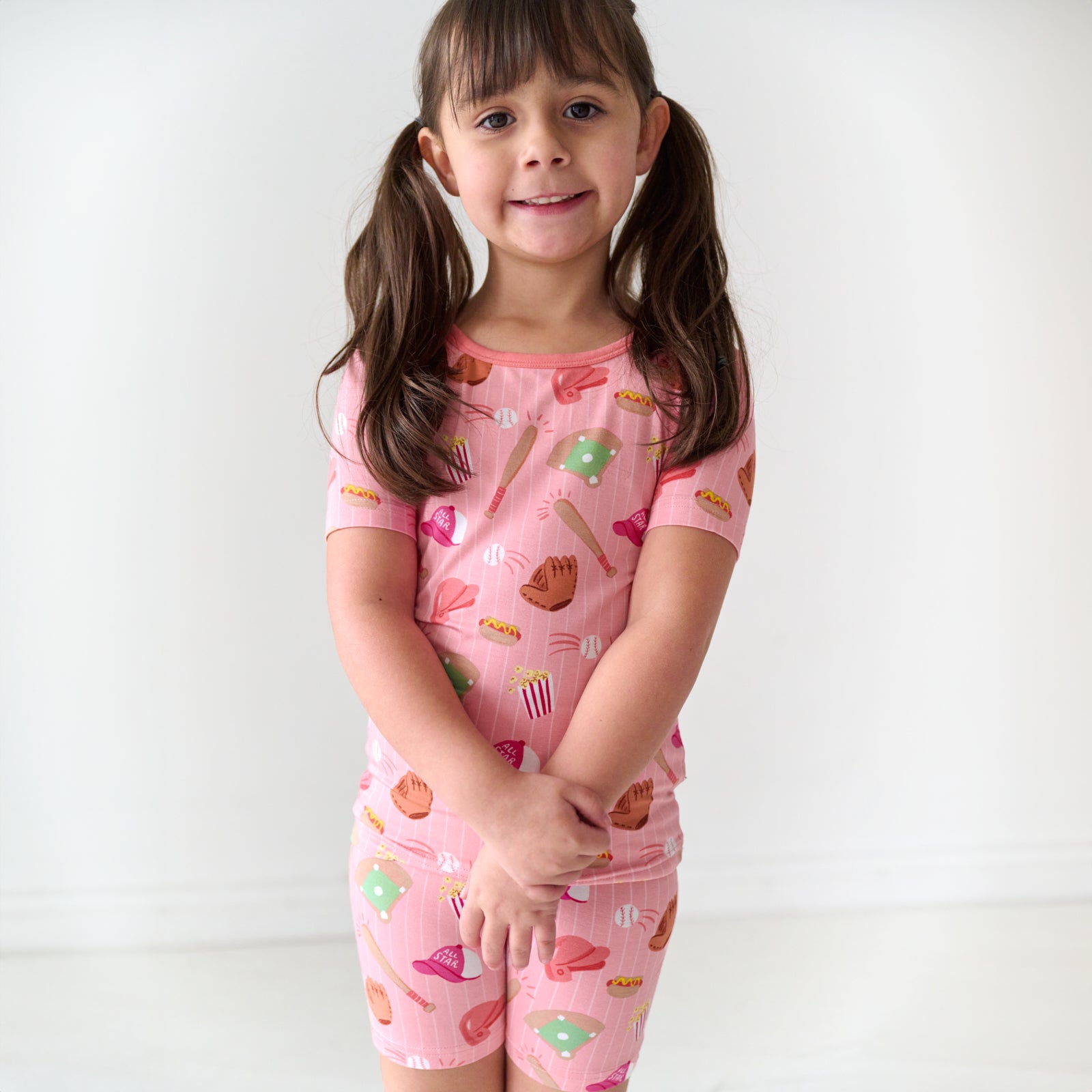 Close up image of a child posing wearing Pink All Stars two piece short sleeve and shorts pajama set