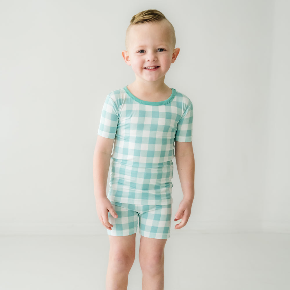 Click to see full screen - Child posing wearing a Aqua Gingham two piece short sleeve and shorts pajama set