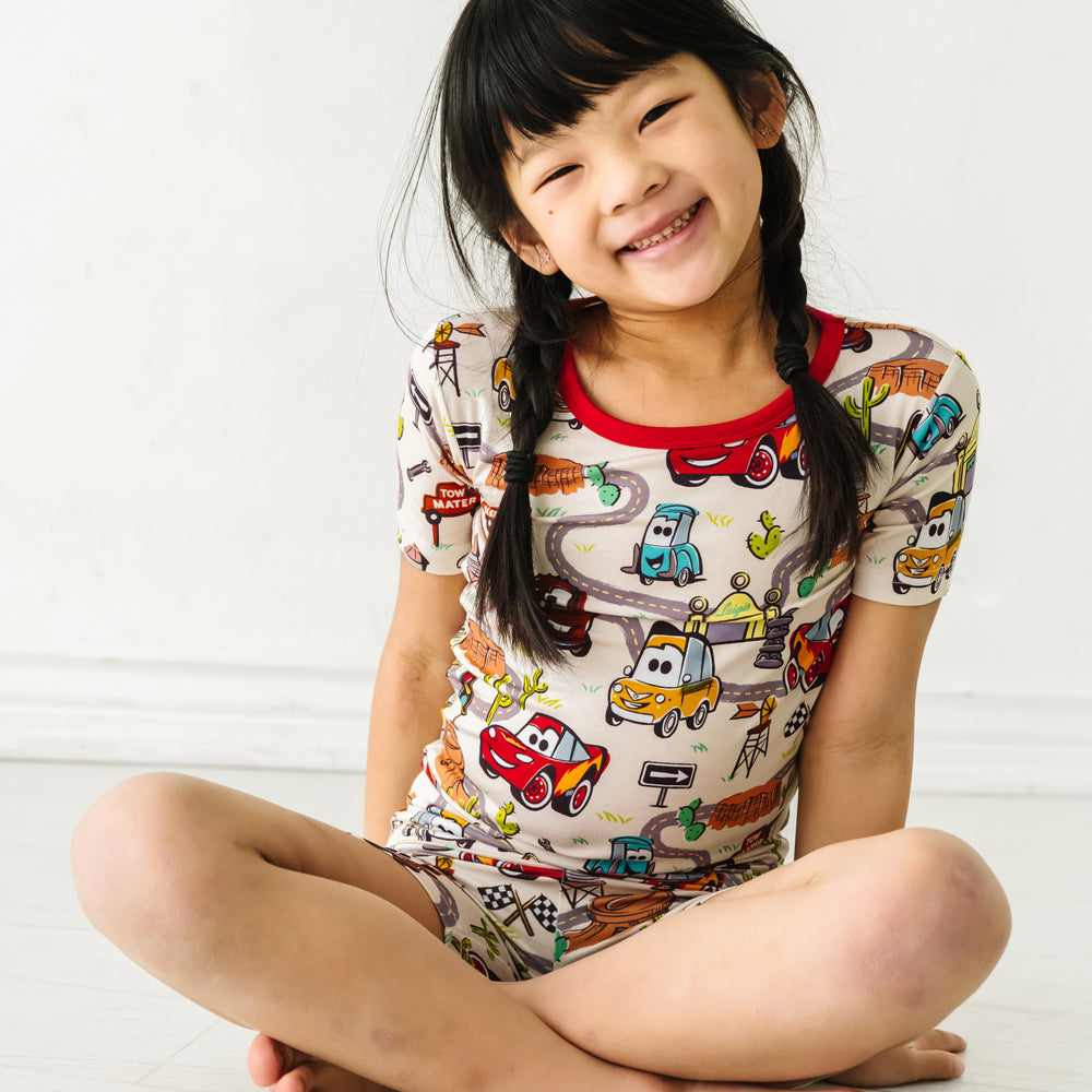 Child sitting wearing Radiator Springs two piece short sleeve and shorts pajama set