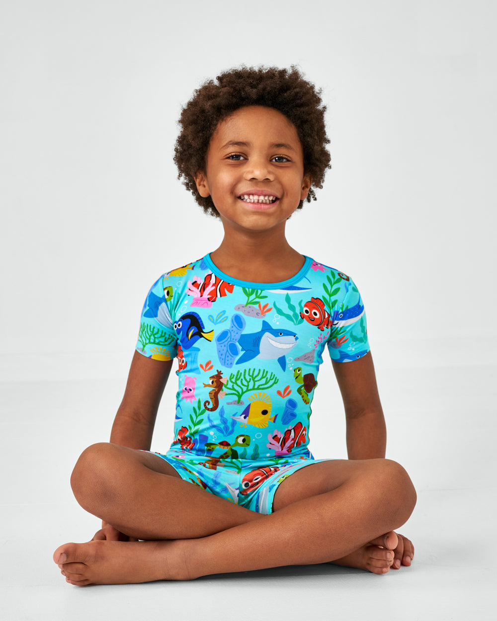 Sitting child wearing the Disney Nemo's Reef Two-Piece Short Sleeve & Shorts bamboo Pajama Set
