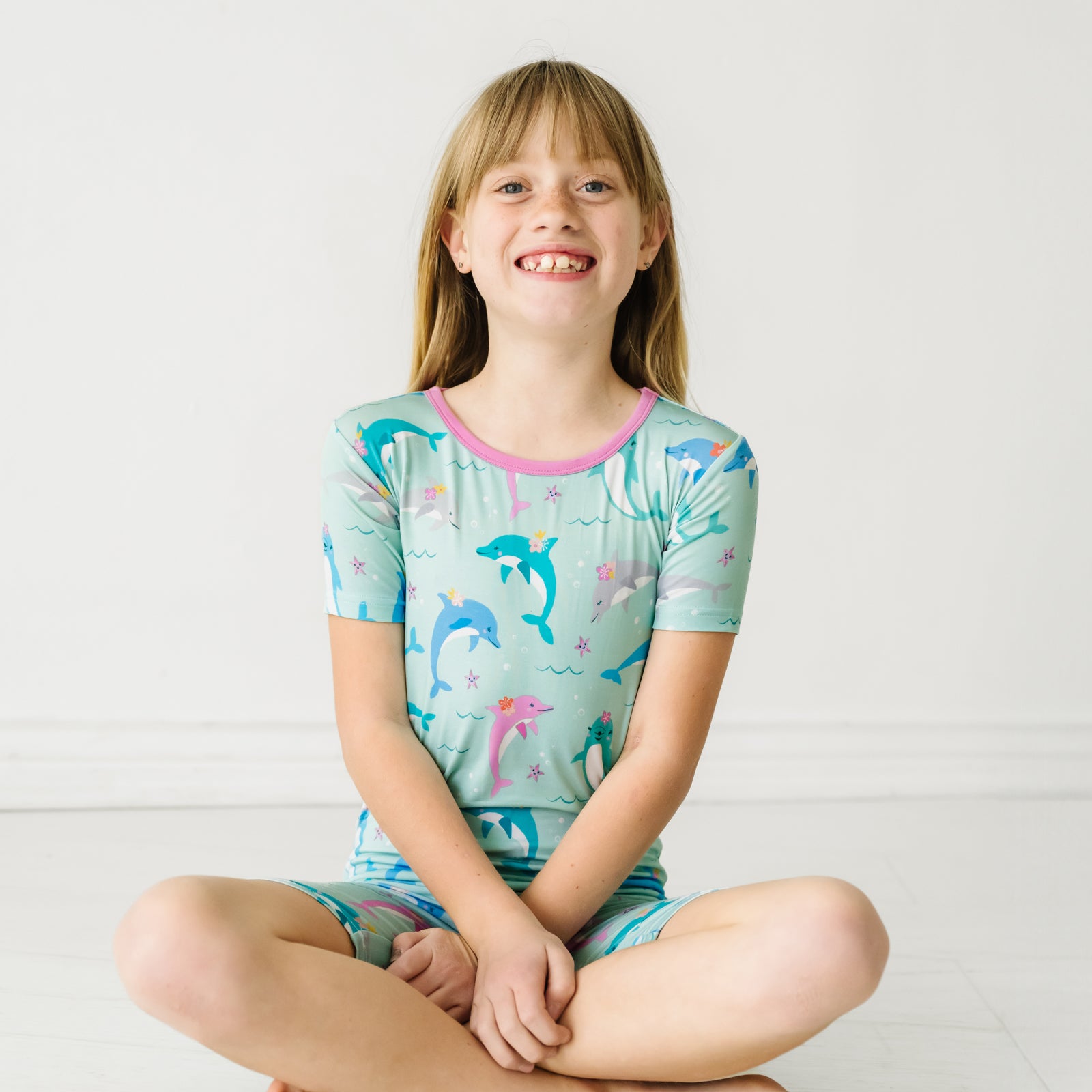 Child sitting on the ground wearing a Dolphin Dance two-piece short sleeve & shorts pajama set