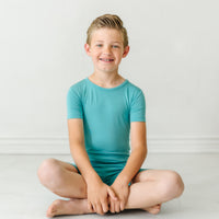 Alternate image of a child sitting wearing a Glacier Turquoise two piece short sleeve and shorts pajama set