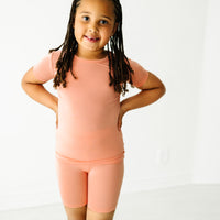 Child posing wearing a Peach two piece short sleeve and shorts pajama set