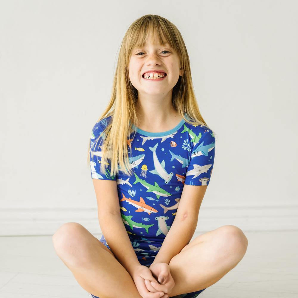 Child sitting on the ground wearing a Rad Reef two-piece short sleeve & shorts pajama set