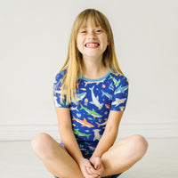 Child sitting on the ground wearing a Rad Reef two-piece short sleeve & shorts pajama set