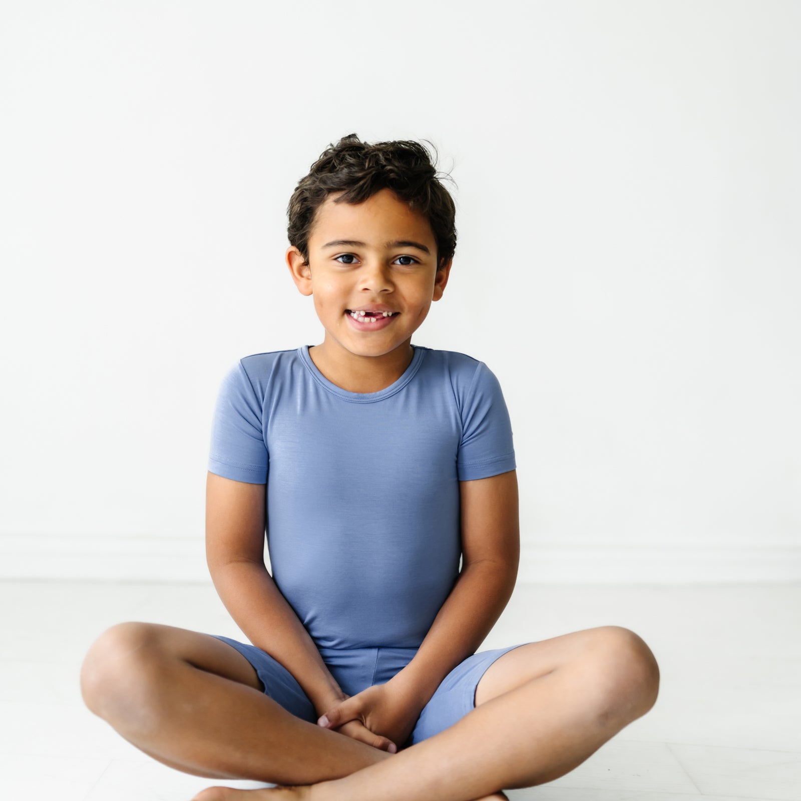 Child sitting wearing Slate Blue two piece short sleeve and shorts pajama set