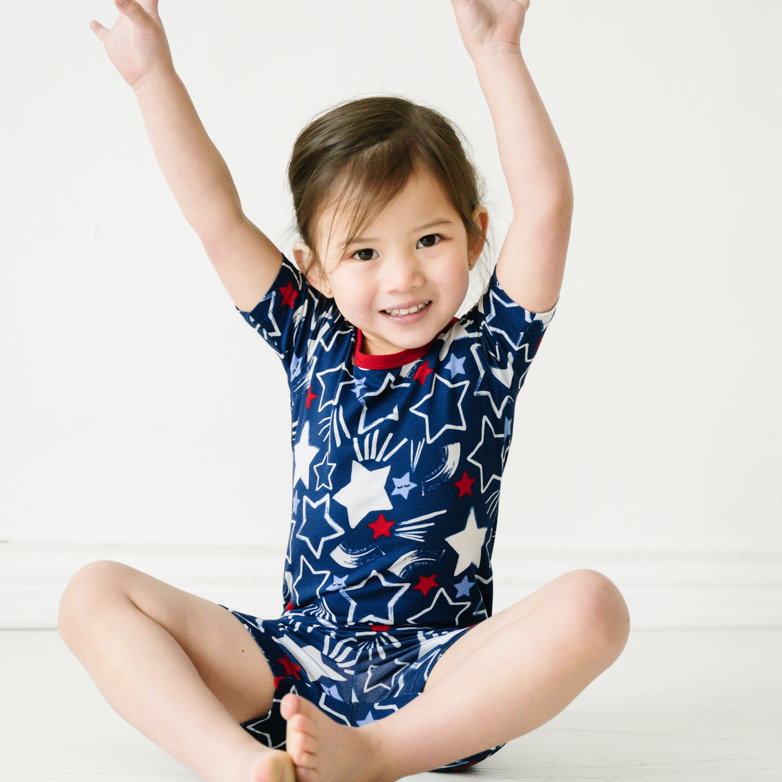 Child sitting wearing a Star Spangled two piece short sleeve and shorts pajama set