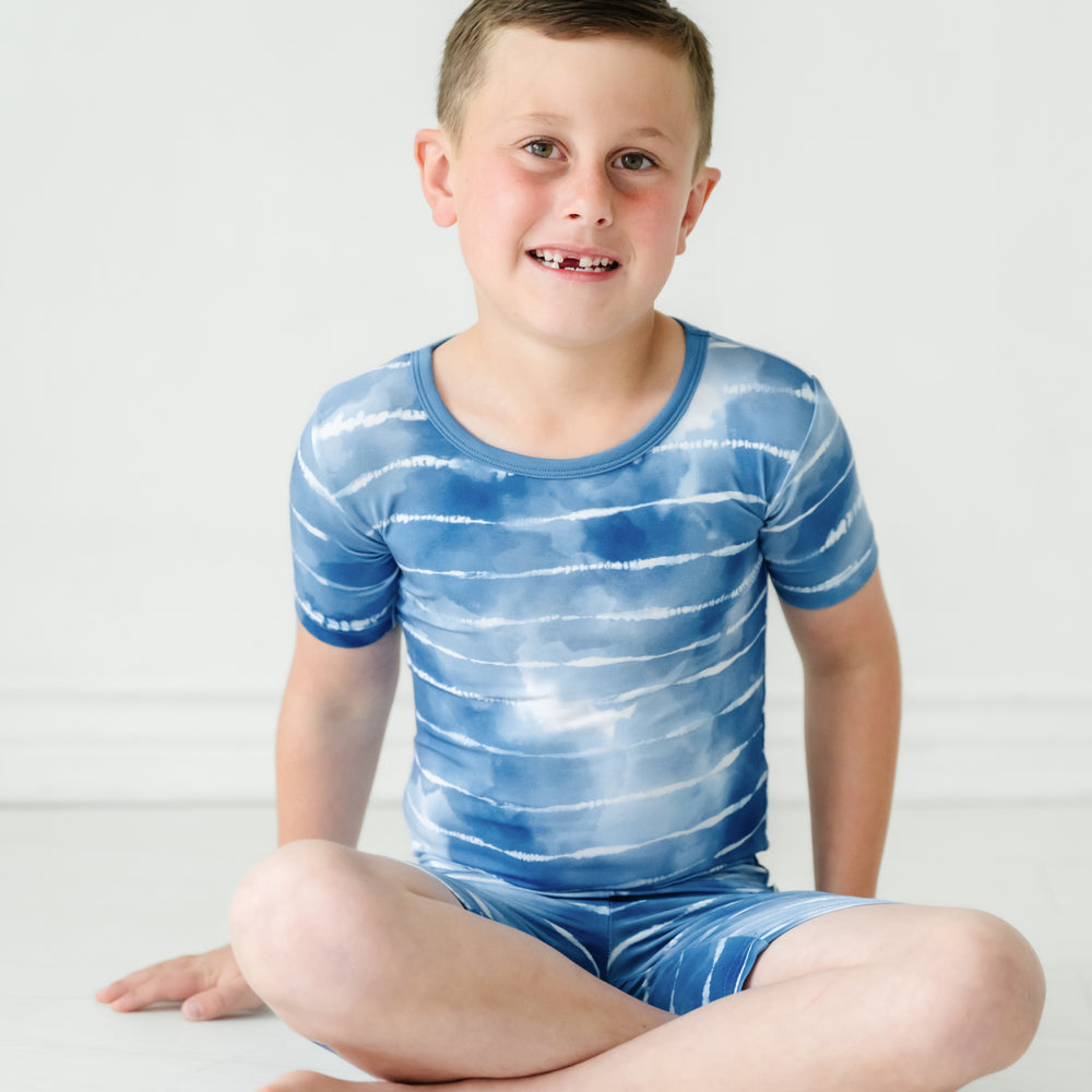 Alternate image of a child sitting on the ground wearing a Blue Tie Dye Dreams two-piece short sleeve & shorts pajama set