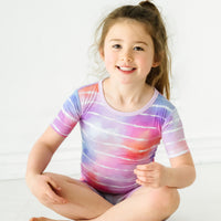 Child sitting on the ground wearing a Pastel Tie Dye Dreams two-piece short sleeve & shorts pajama set