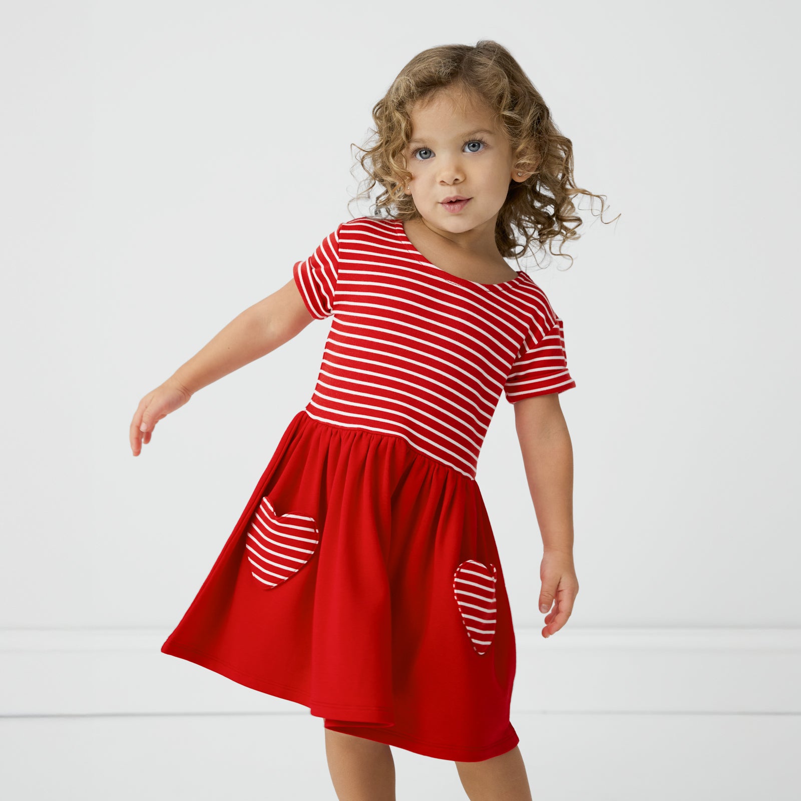 Child leaning to the side wearing a Candy Red Patch Pocket Dress